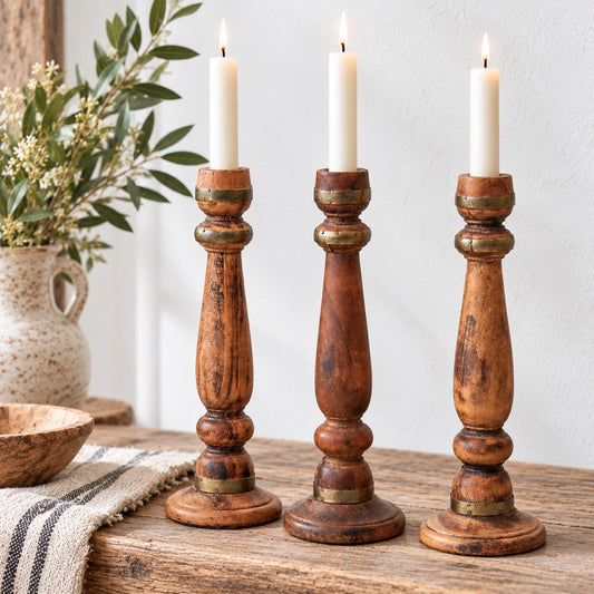 Three wooden candle holders with lit candles are placed on a wooden surface, accompanied by a vase of flowers and a striped cloth.