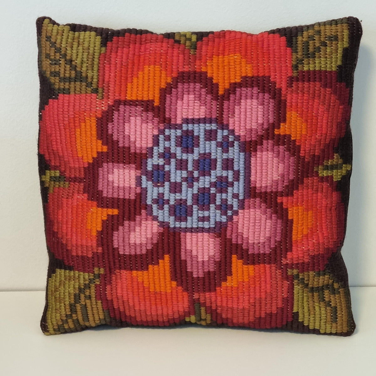 A colorful, hand-knitted or crocheted pillow with a large, intricate flower design in shades of red, orange, and pink.