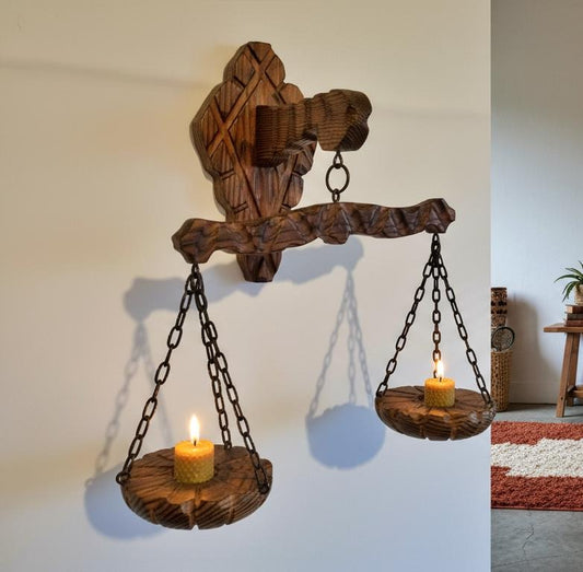 Rustic wooden wall scale candle holder with trays on chains holding lit candles in cozy room setting