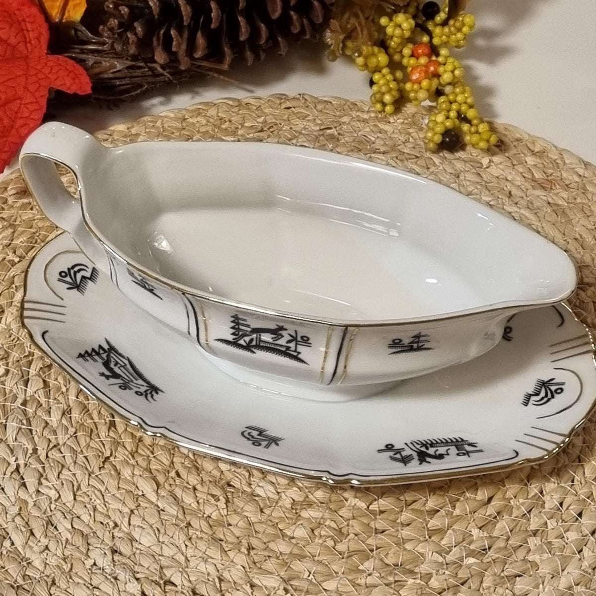 a white ceramic gravy boat and a matching saucer with black designs, placed on a woven placemat.