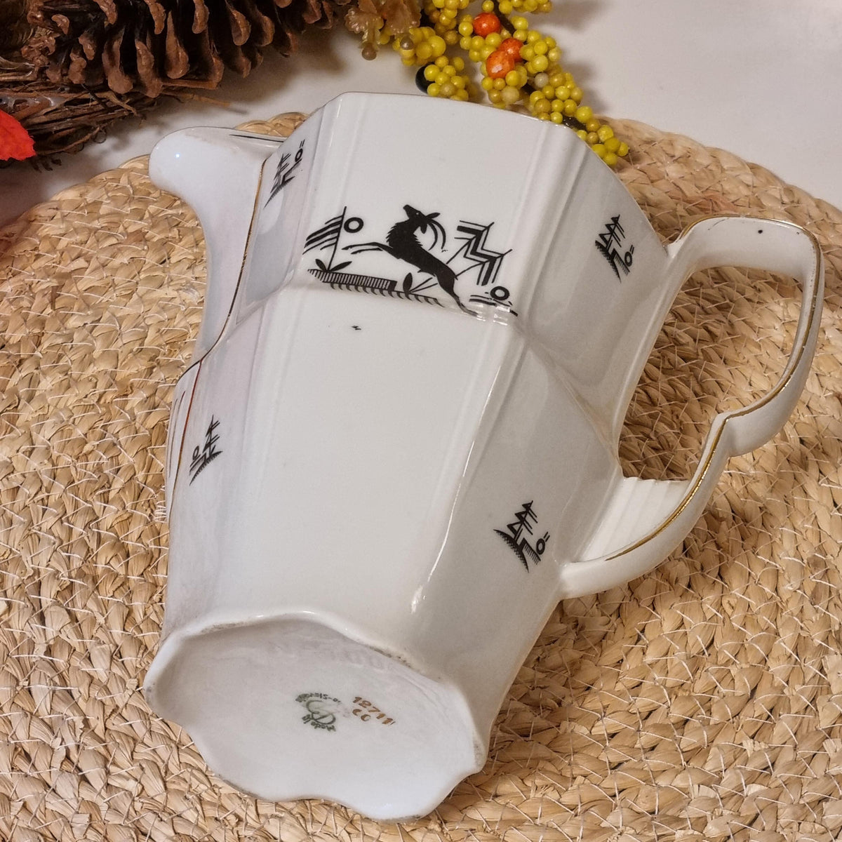 a white ceramic pitcher with black designs on it, placed on a woven mat.