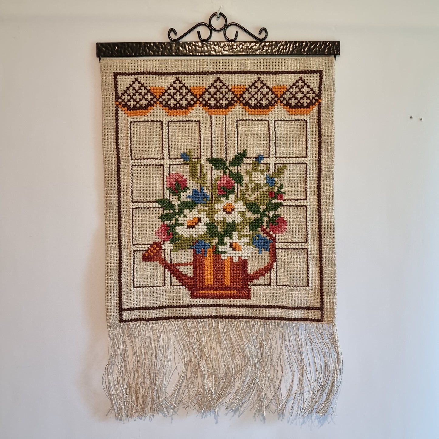 Full view of vintage Swedish cross-stitch floral wall hanging with cream fringe and wrought iron rod