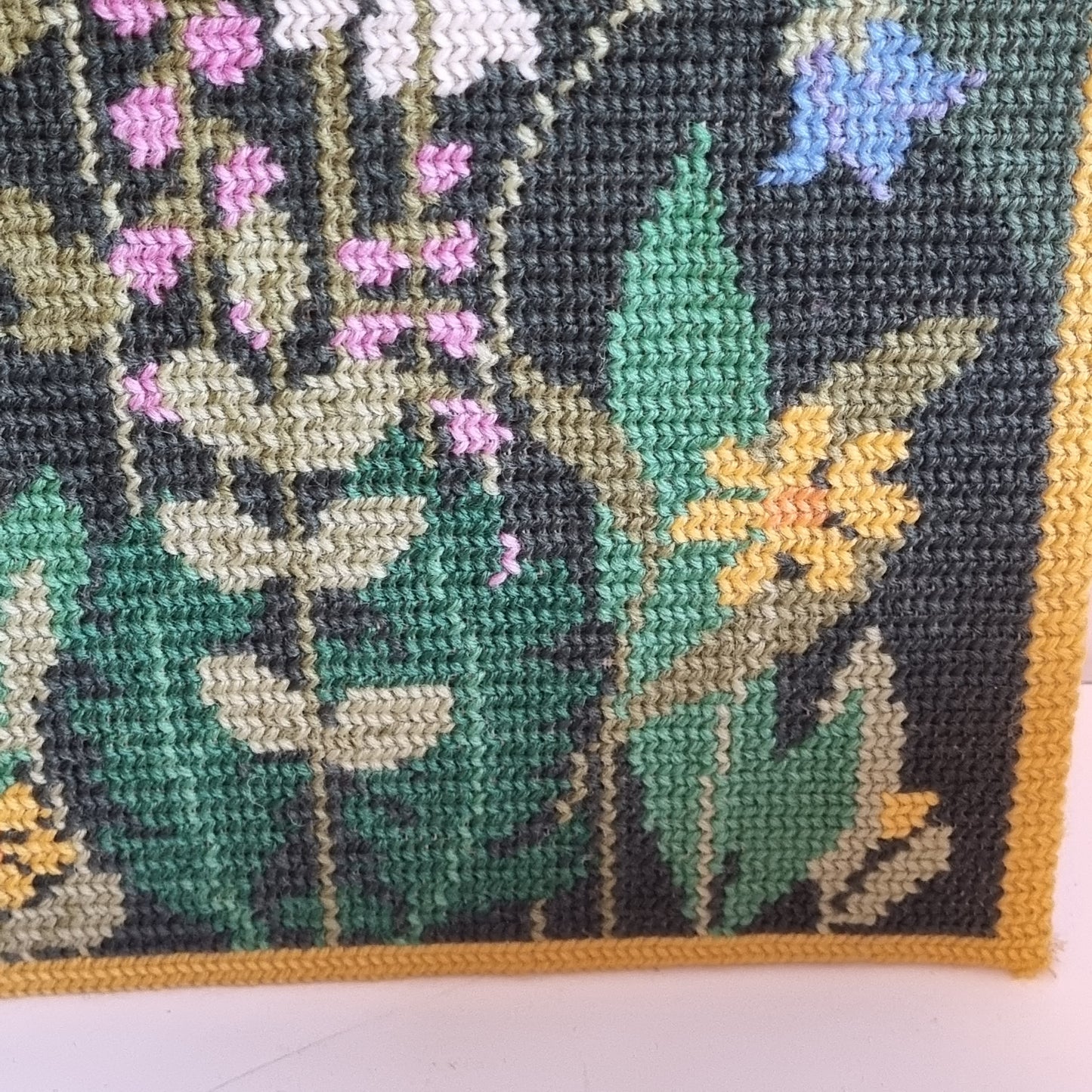 Close-up detail of red poppies and mixed wildflowers on dark green needlepoint ground