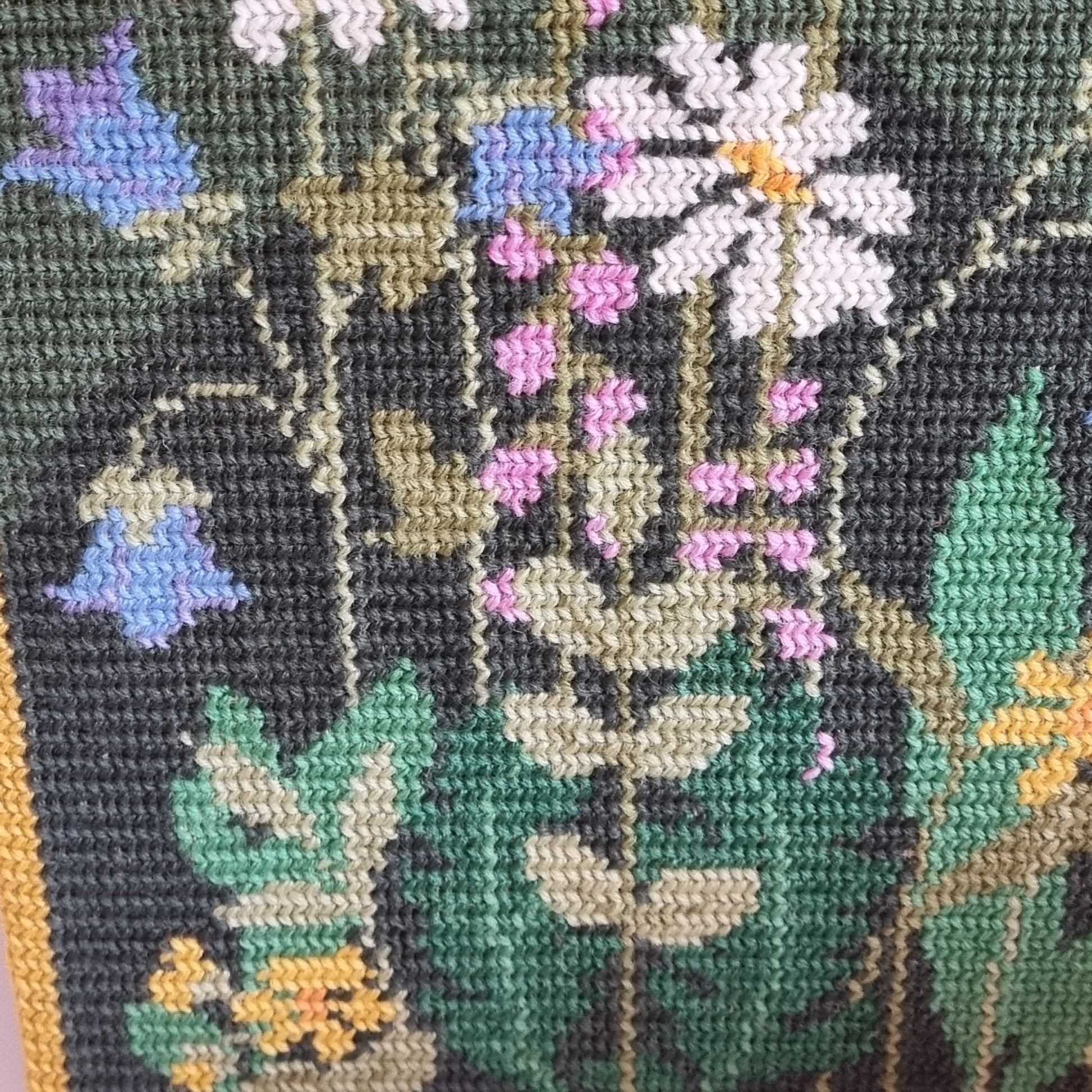 Close-up detail of lilac, blue and white flowers in needlepoint on forest green wool canvas