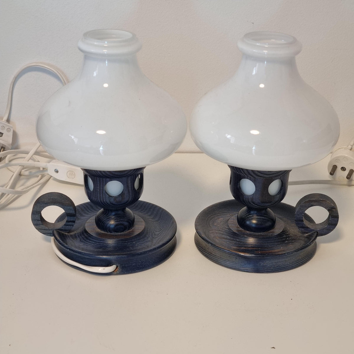 two black and white lamps with wooden bases, placed side by side on a white wall.