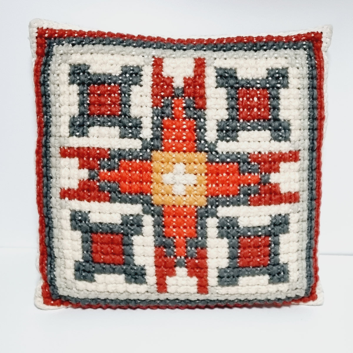 Vintage square embroidered pillow with red and charcoal gray geometric motifs on a cream background