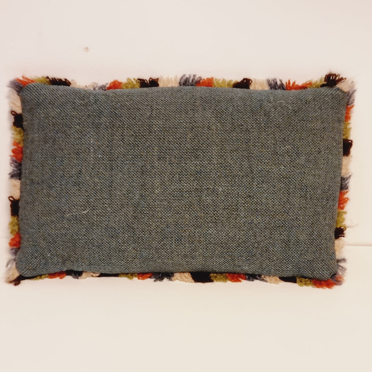 Plain gray fabric back of the small fringed embroidered pillow