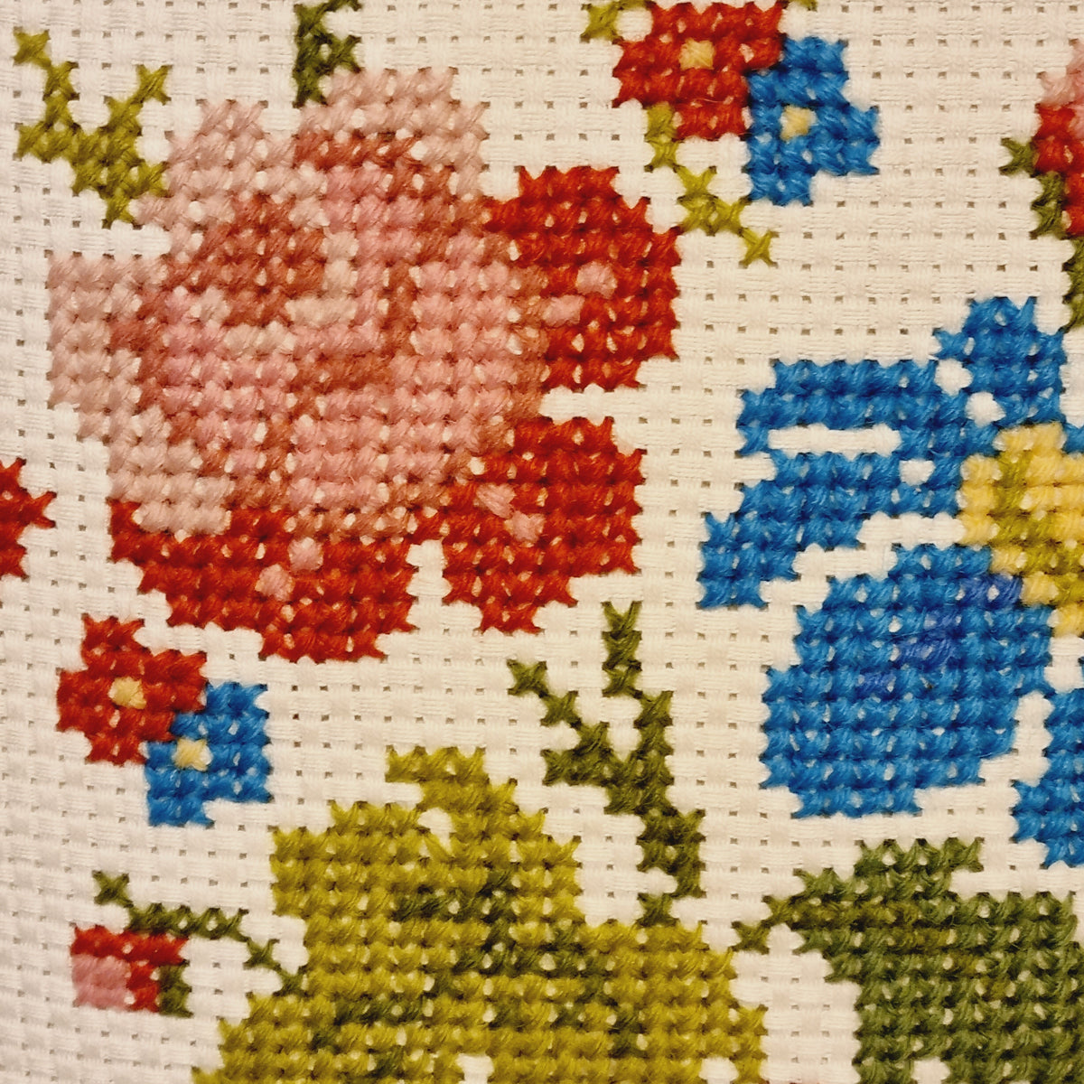 Close-up of the floral cross-stitch embroidery in pink, red, blue and olive green