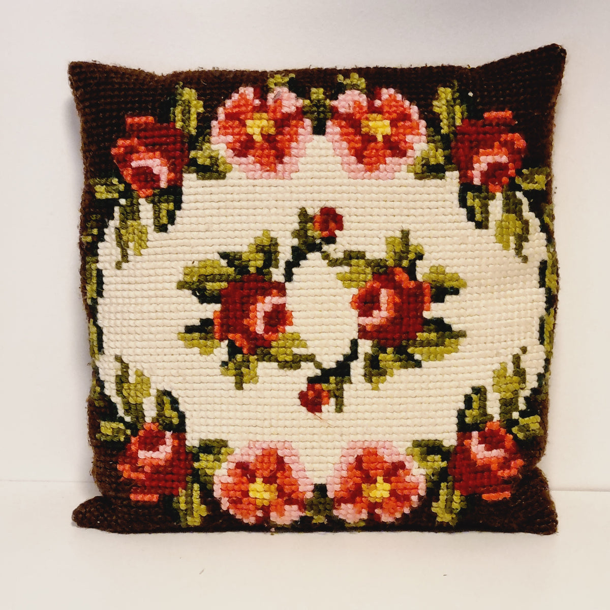 Vintage needlepoint pillow with red roses in a cream center and a red and pink floral border on dark brown