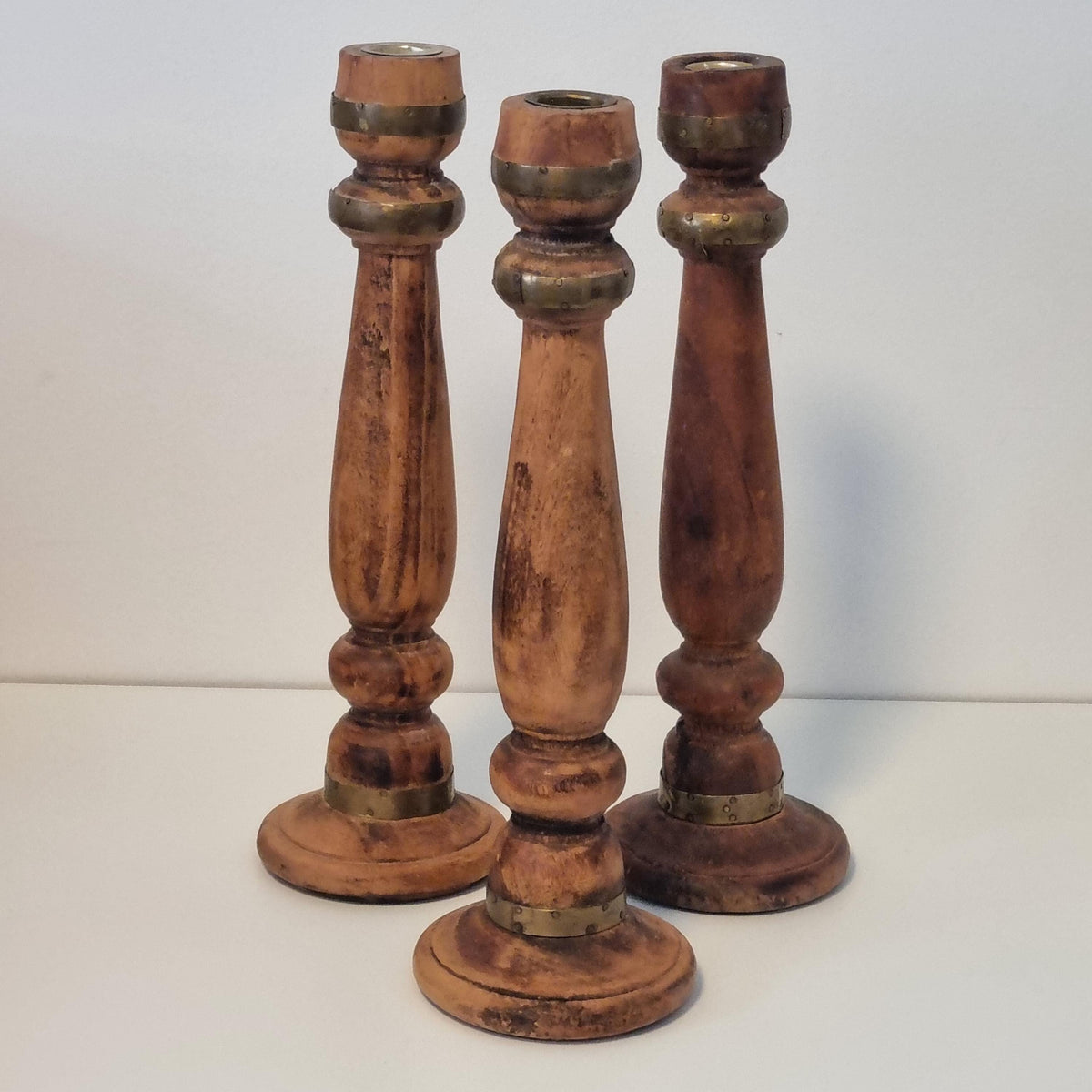 Three wooden candle holders with brass accents, arranged in a row against a white background.