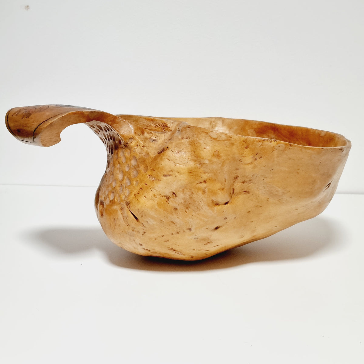 Hand carved burl bowl with curved handle, profile view