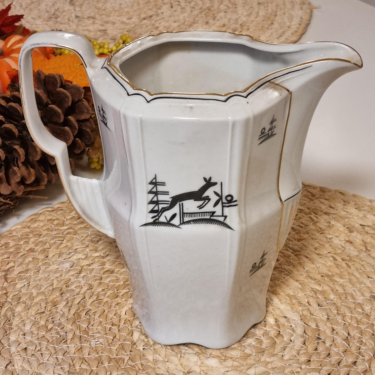 a white ceramic pitcher with a black design on it, placed on a woven placemat.