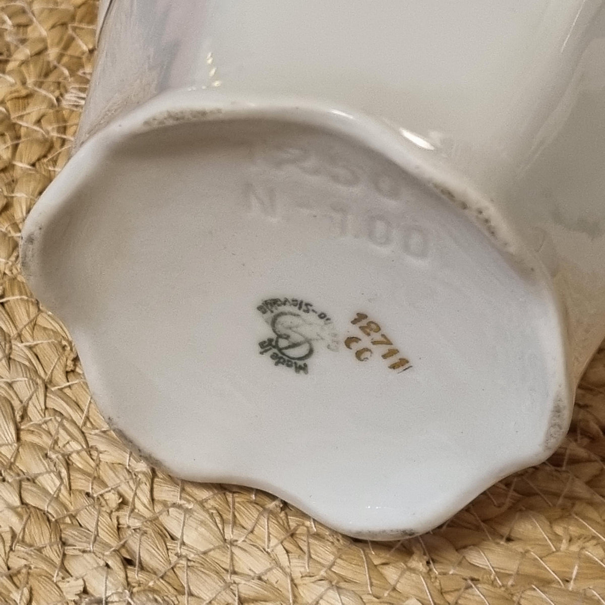 a close-up view of a white ceramic vase or container with a small, embossed logo or marking on it.