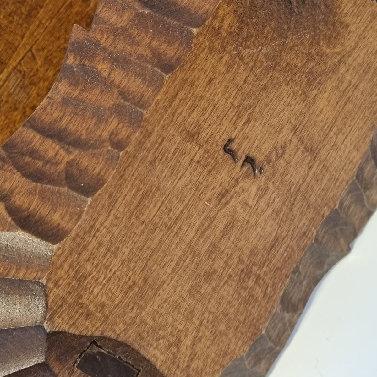 a close-up view of a wooden surface with a dark brown, textured appearance. There is a small, dark object, possibly a screw or nail, visible in the center of the image.