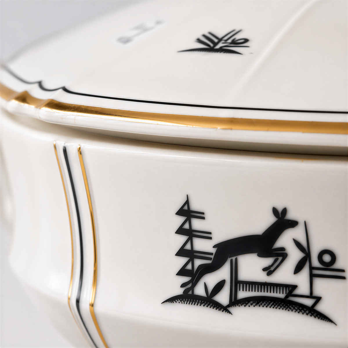 a close-up view of a white ceramic bowl with a gold trim. The bowl has a black silhouette of a deer and some other decorative elements on its surface.