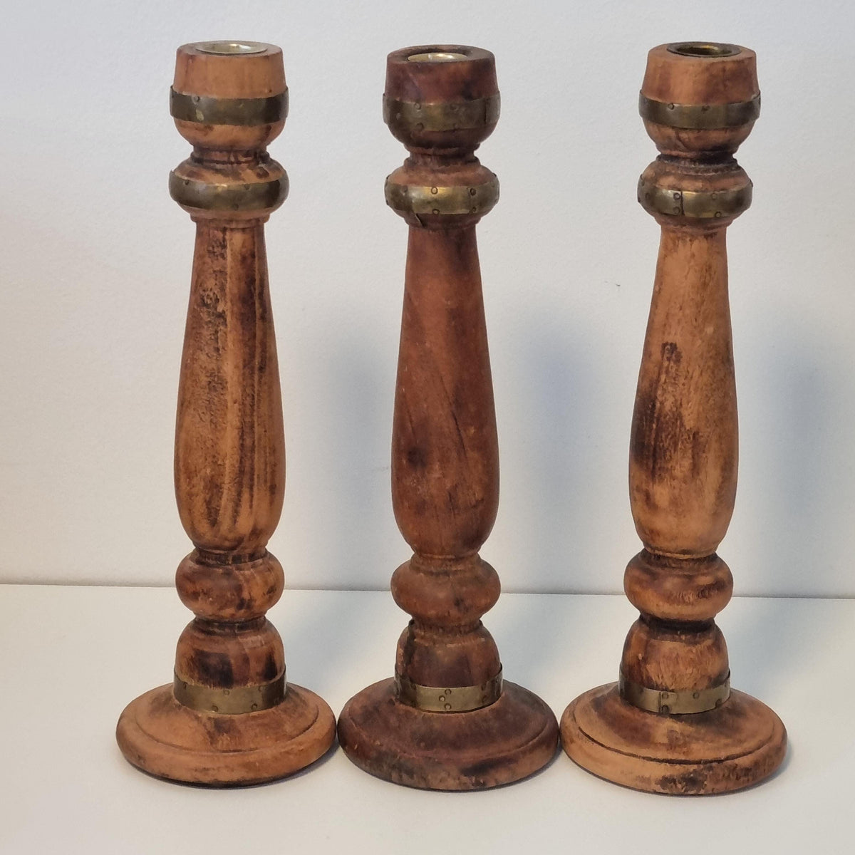 Three wooden candle holders with brass accents, arranged in a row against a white background.