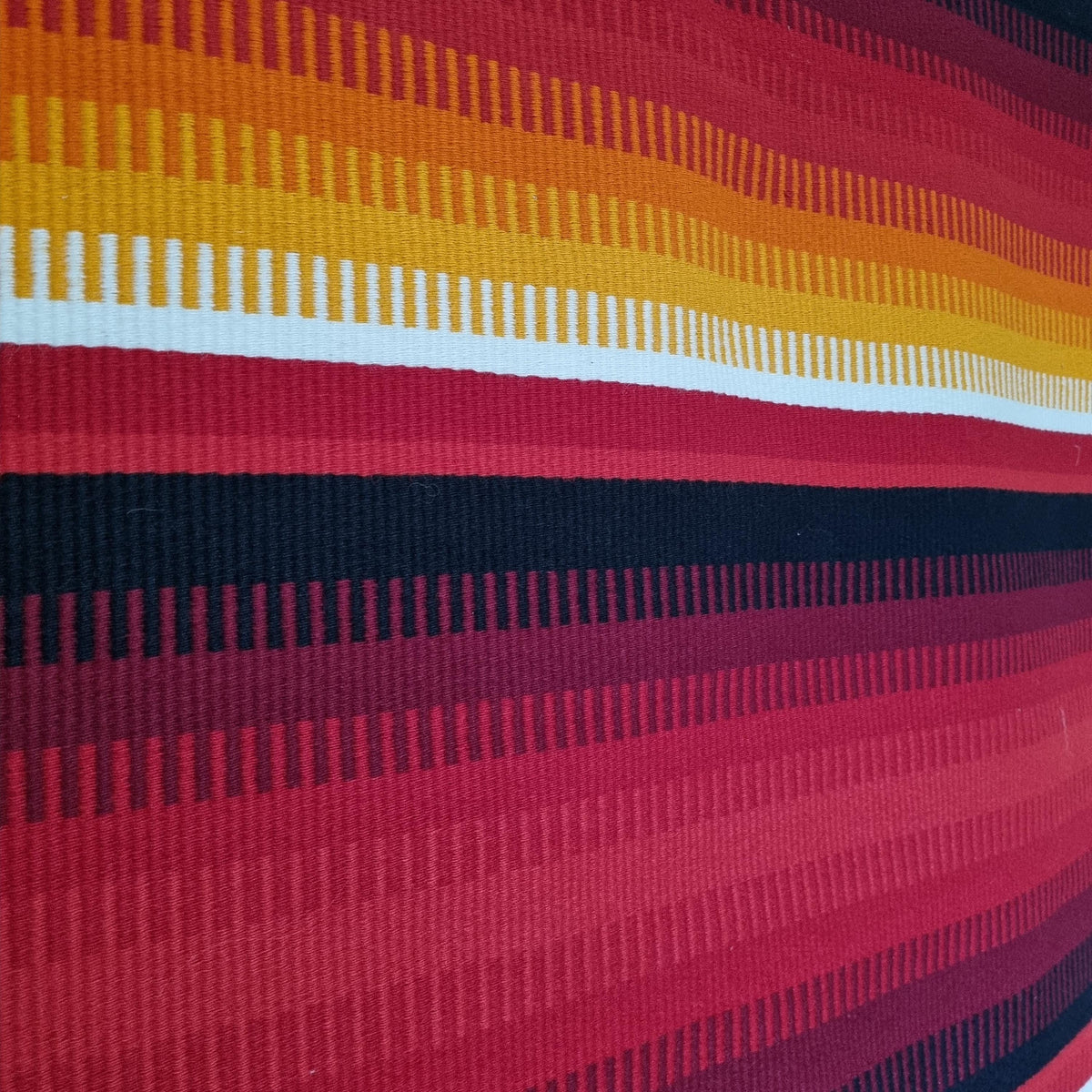 a close-up view of a vibrant, multicolored textile with vertical stripes in red, orange, yellow, and black.