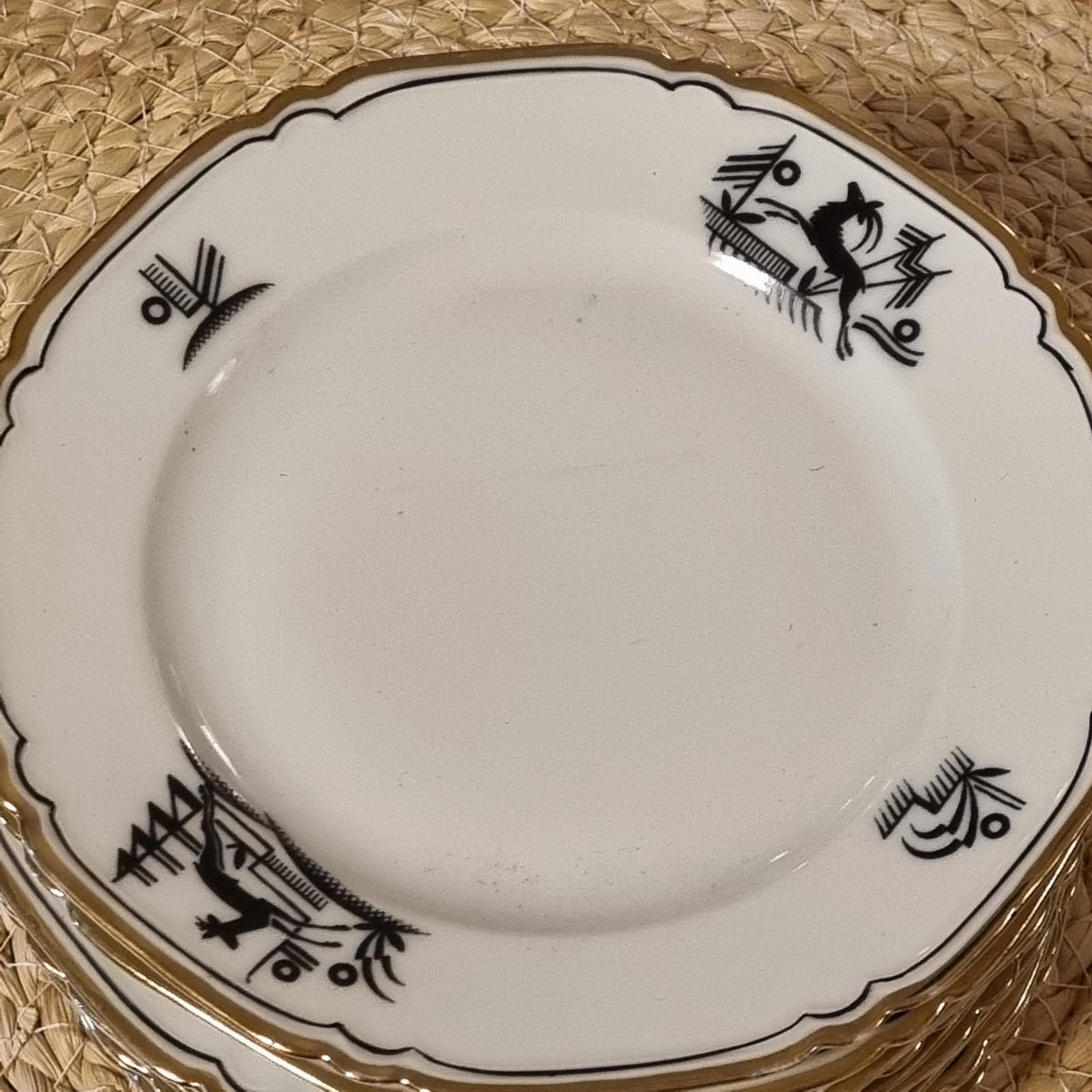 a white plate with black designs on it, placed on a woven mat.