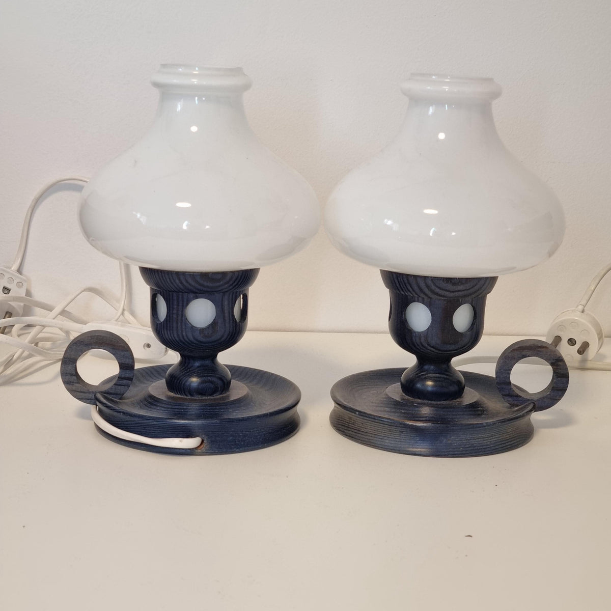 two black and white lamps with white shades, placed side by side on a white wall.