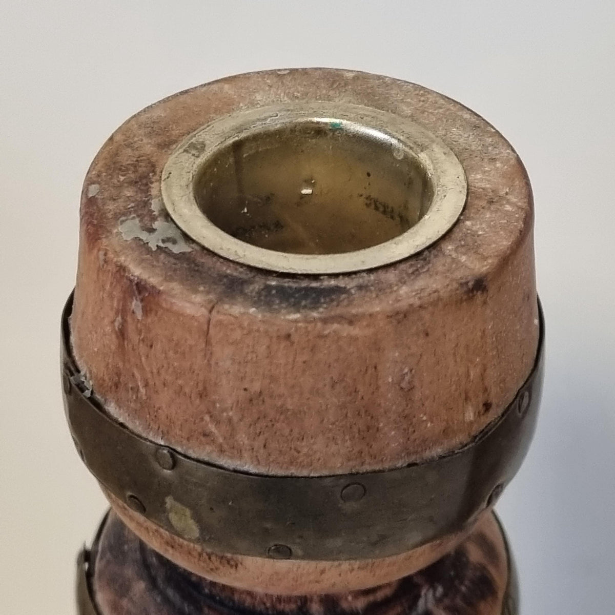 a close-up view of a wooden object with a metal ring or cover attached to it, possibly a candle holder or a similar decorative piece.