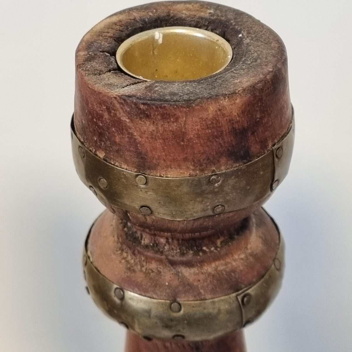 A close-up view of a wooden and metal object, possibly a candle holder or a decorative piece, with a yellow-colored candle inserted in it.
