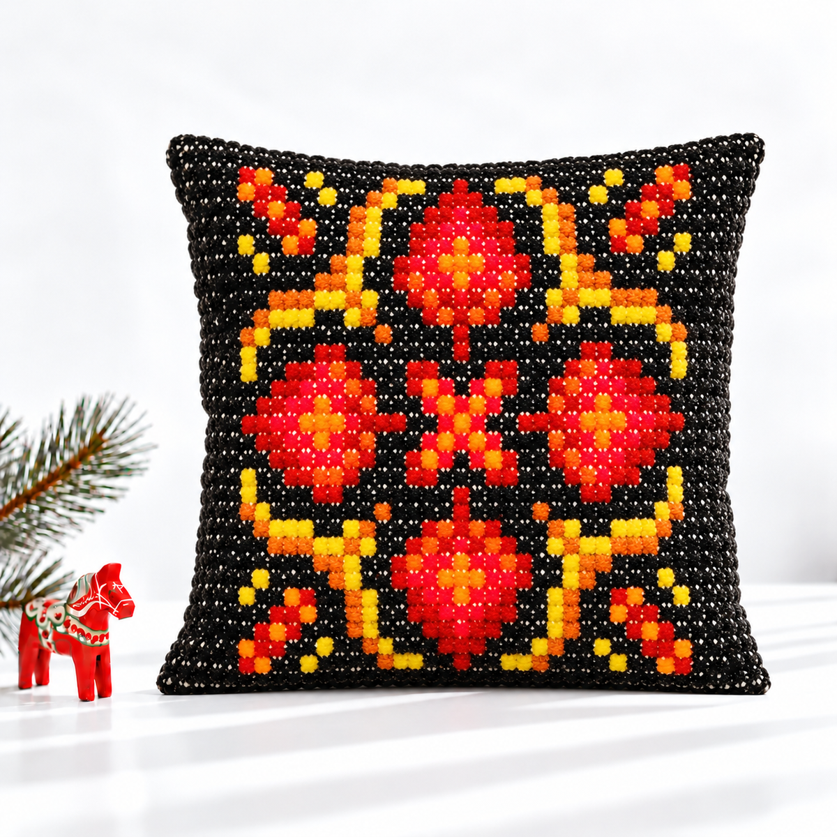 Red and black geometric embroidered pillow styled with a red Dala horse and evergreen branch
