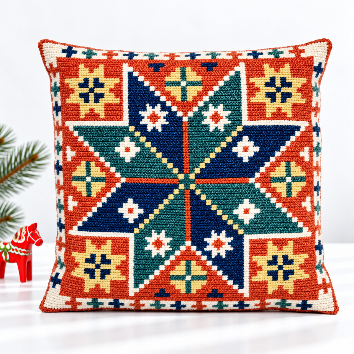 Geometric embroidered star pillow styled with a red Dala horse and evergreen branch