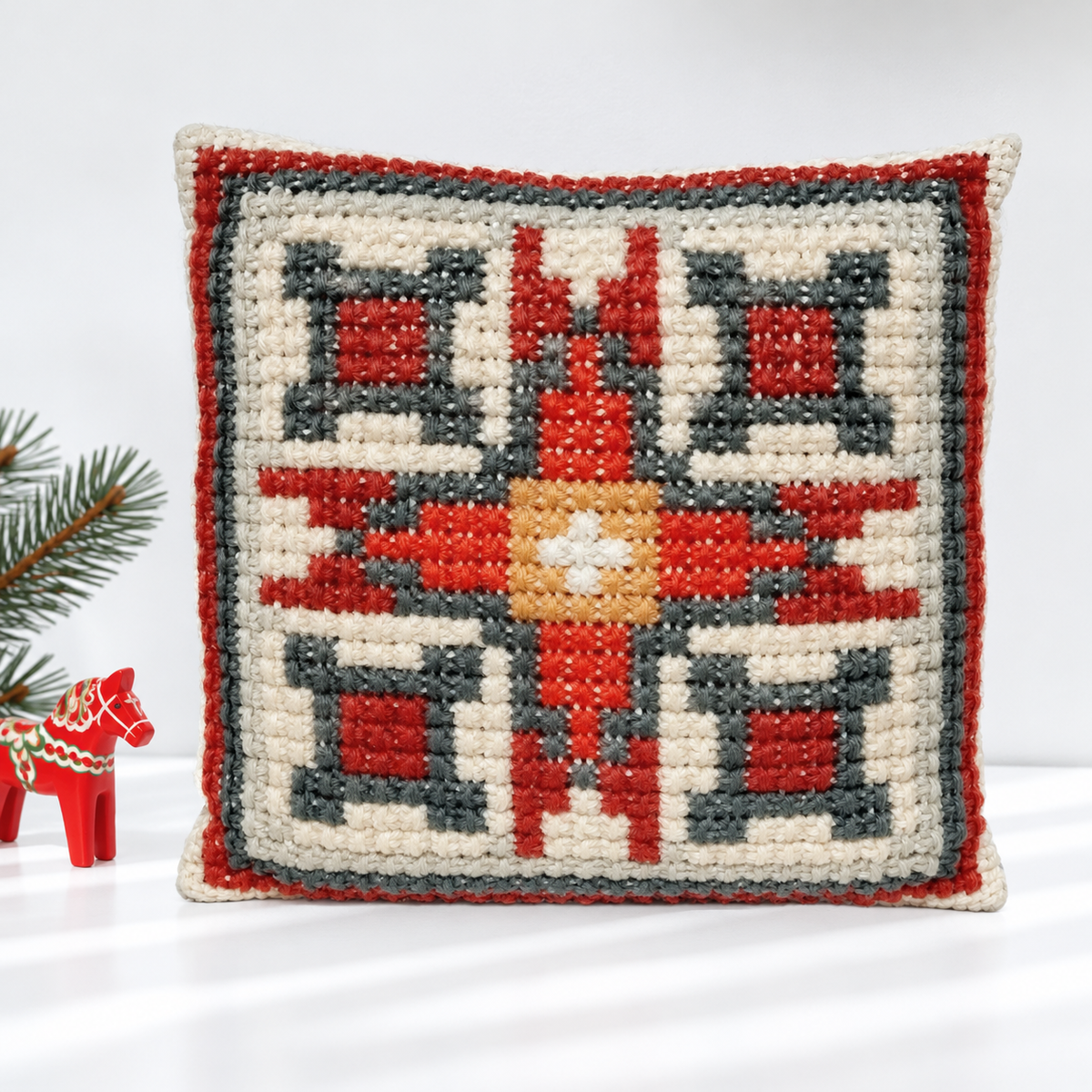Red and gray geometric embroidered pillow styled with a red Dala horse and evergreen branch