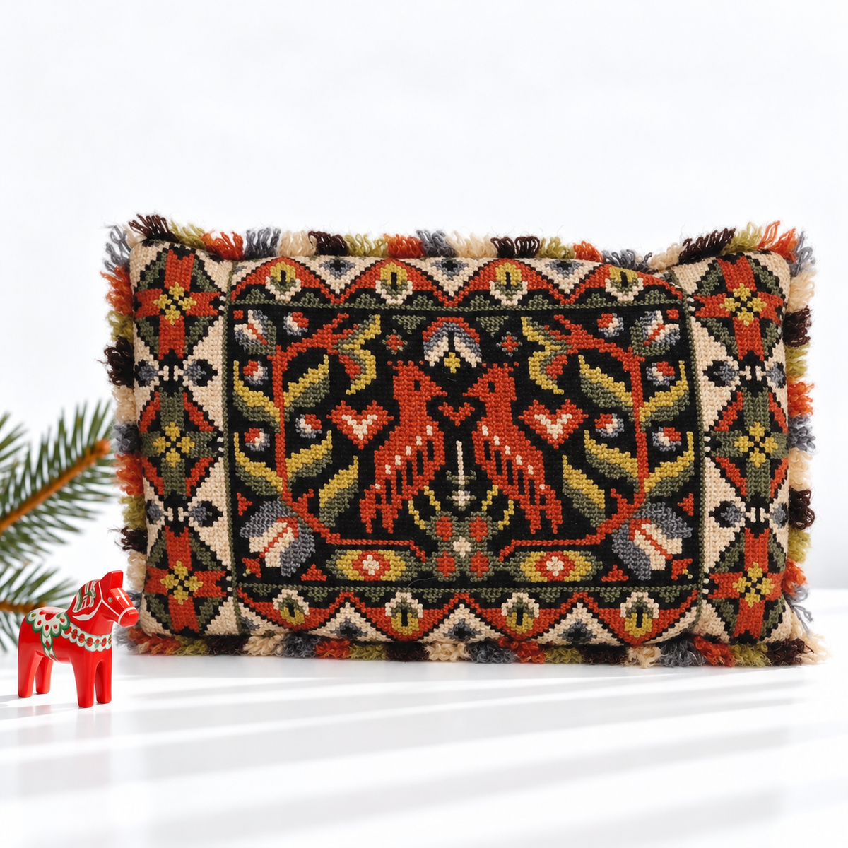 Fringed bird embroidered pillow styled with a red Dala horse and evergreen branch