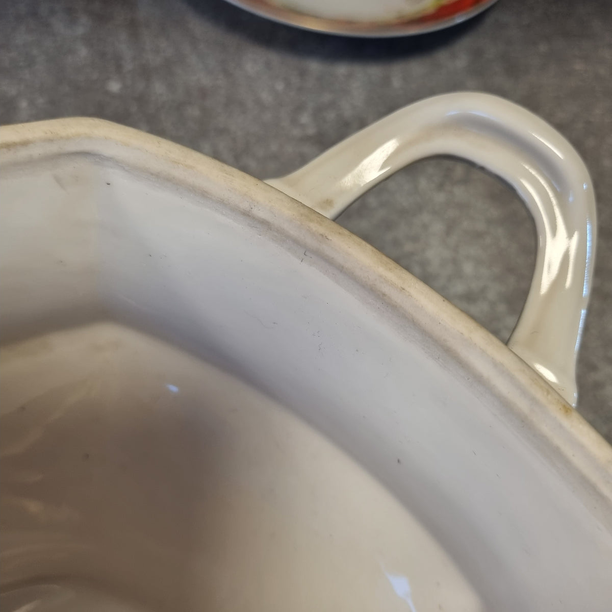 A close-up view of a white ceramic bowl with a curved handle, resting on a gray surface.