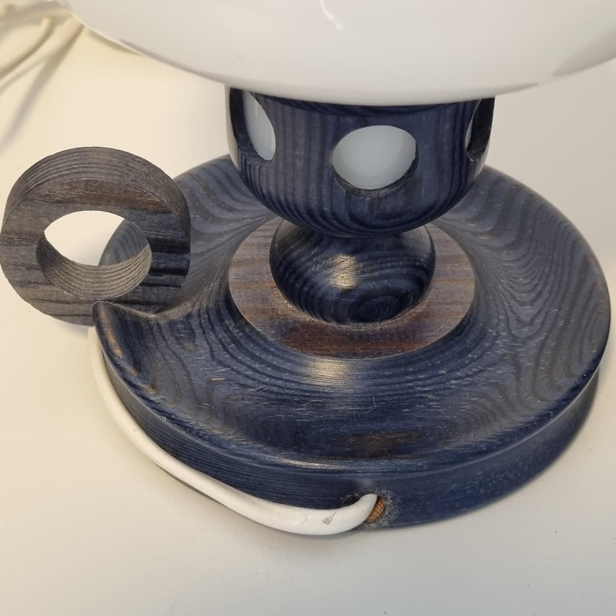 a wooden lamp base with a blue finish, featuring a circular hole and a white cord attached to it.