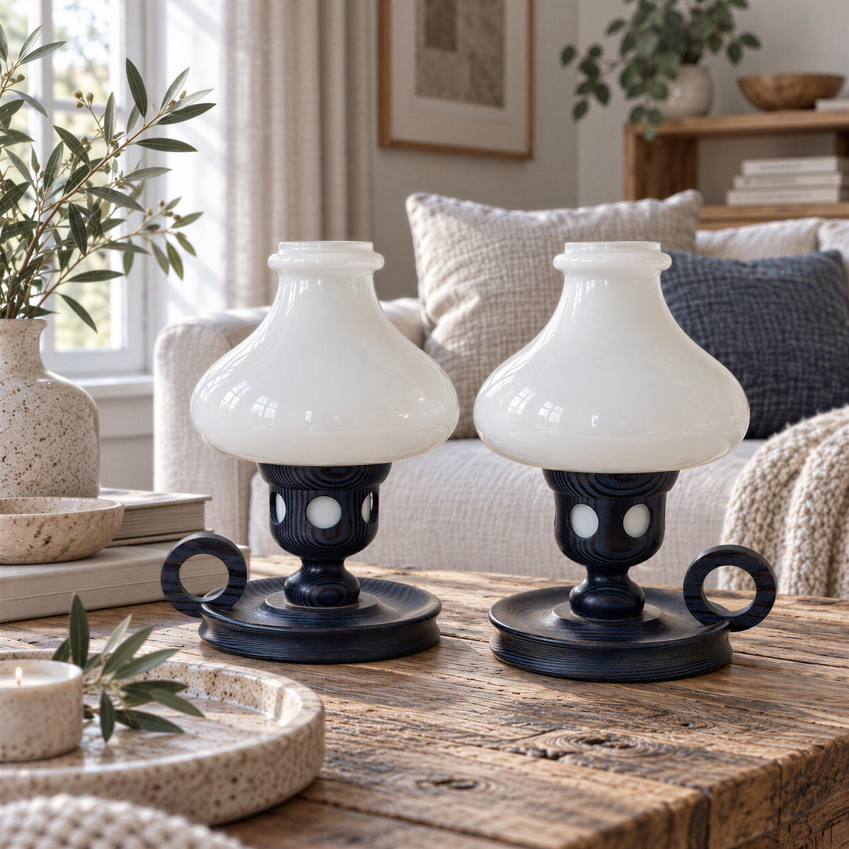 two white lamp bases with black handles, placed on a wooden table in a cozy living room setting.