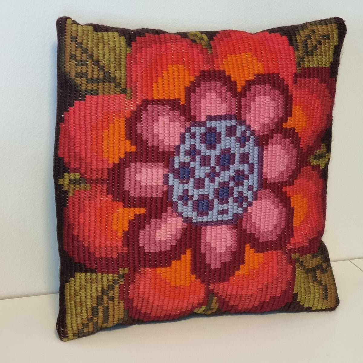 A colorful, hand-stitched pillow with a large, intricate flower design in shades of red, orange, and blue.