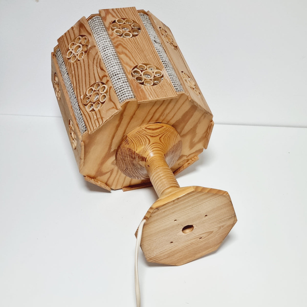 A wooden lamp with a hexagonal base and a circular design on the front, mounted on a white wall.
