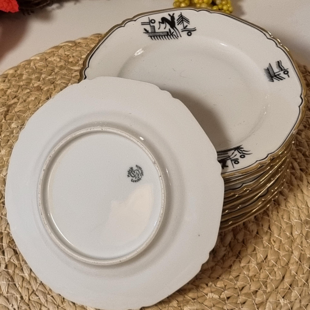 A stack of white plates with black designs on them, placed on a woven mat.