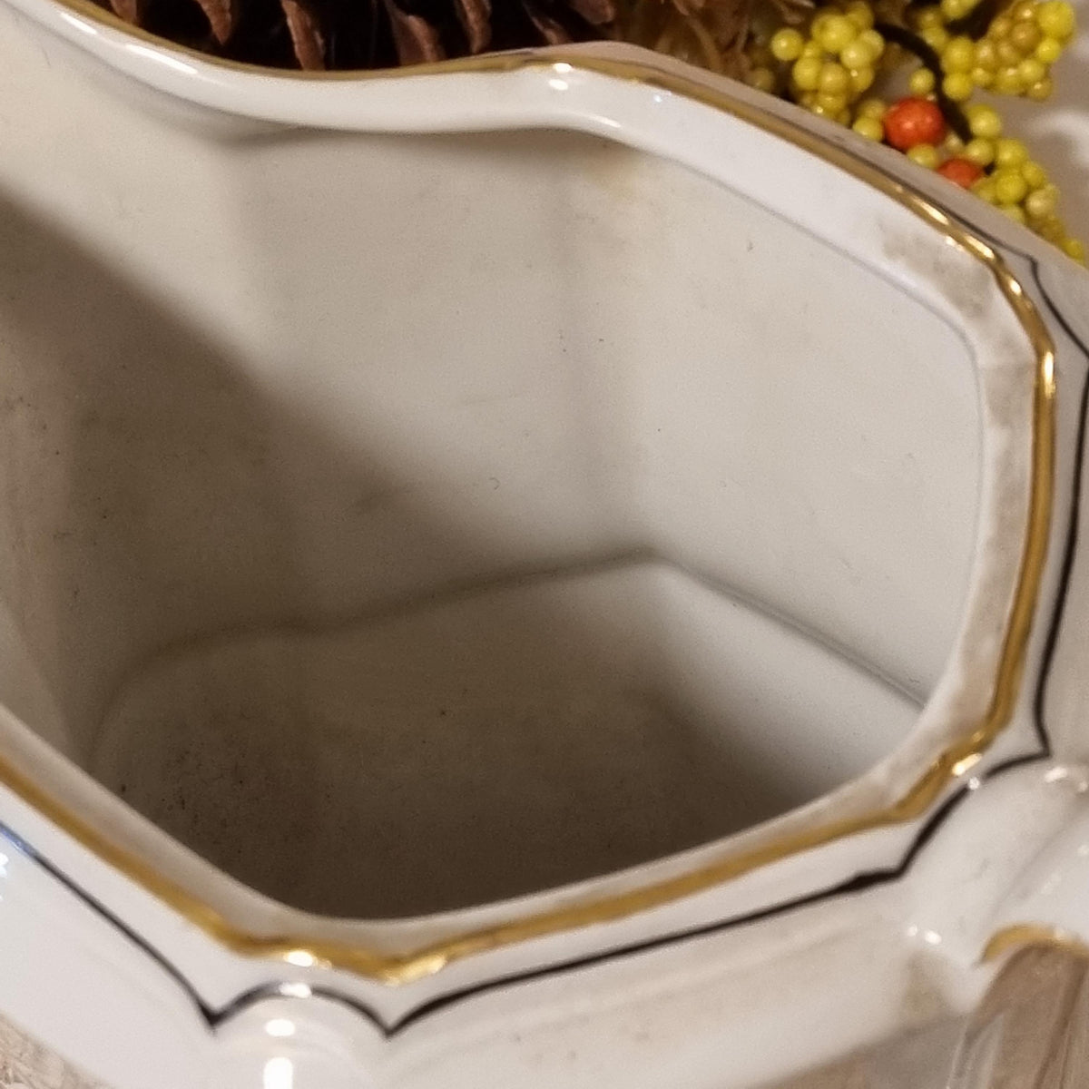 a close-up view of a white ceramic pitcher with a gold trim, placed on a surface with a blurred background.