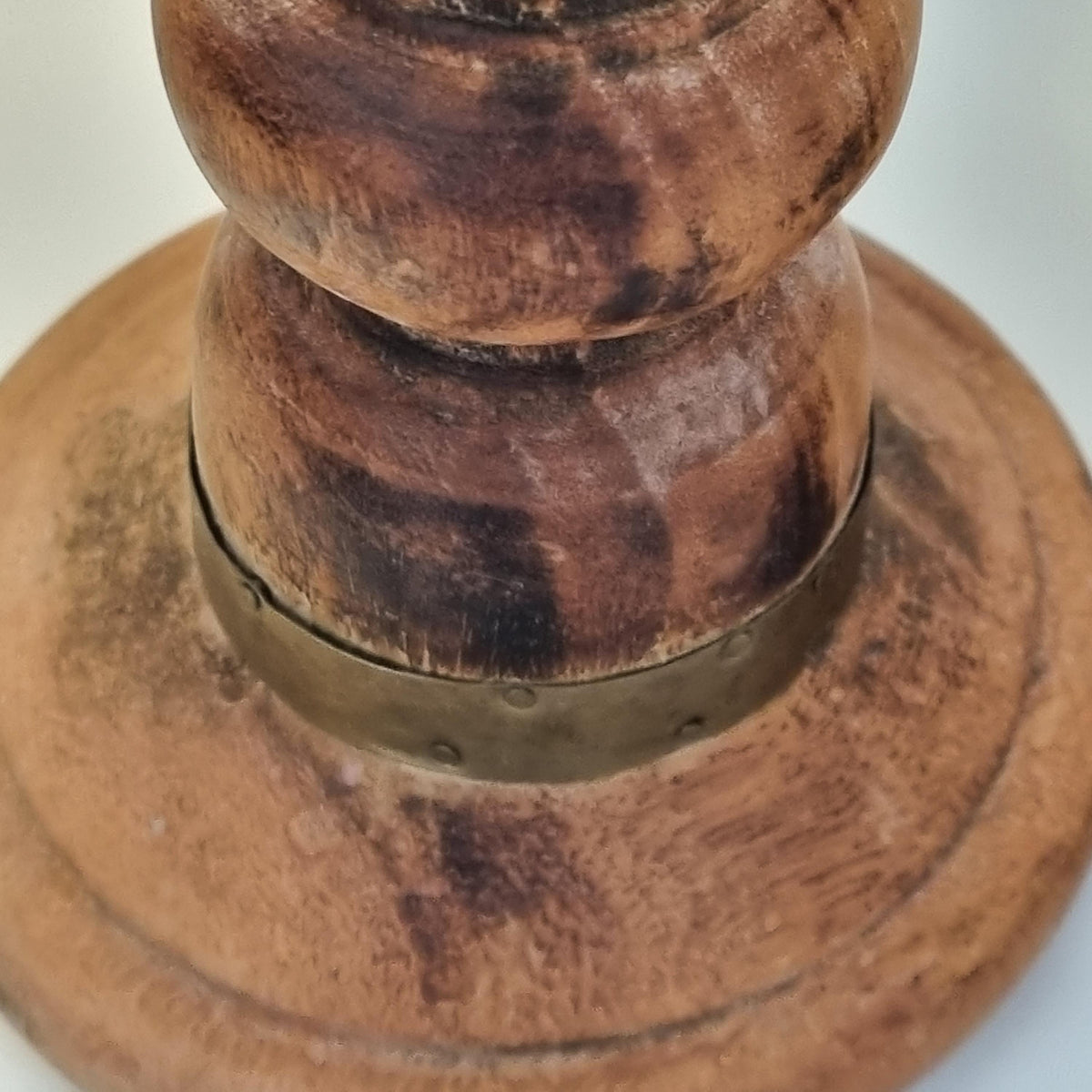 A close-up view of a wooden object, possibly a piece of furniture or a decorative item, with a metal band or clasp attached to it.