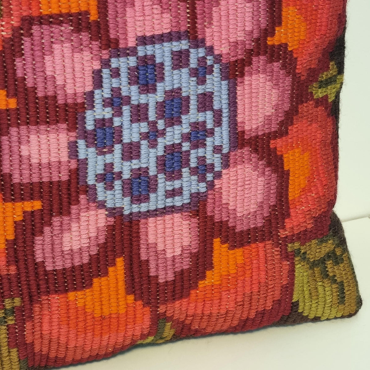 a vibrant, hand-knitted or crocheted pillow with a large, colorful flower design. The flower is composed of numerous small, circular shapes in shades of pink, orange, and blue, creating a visually striking and intricate pattern.