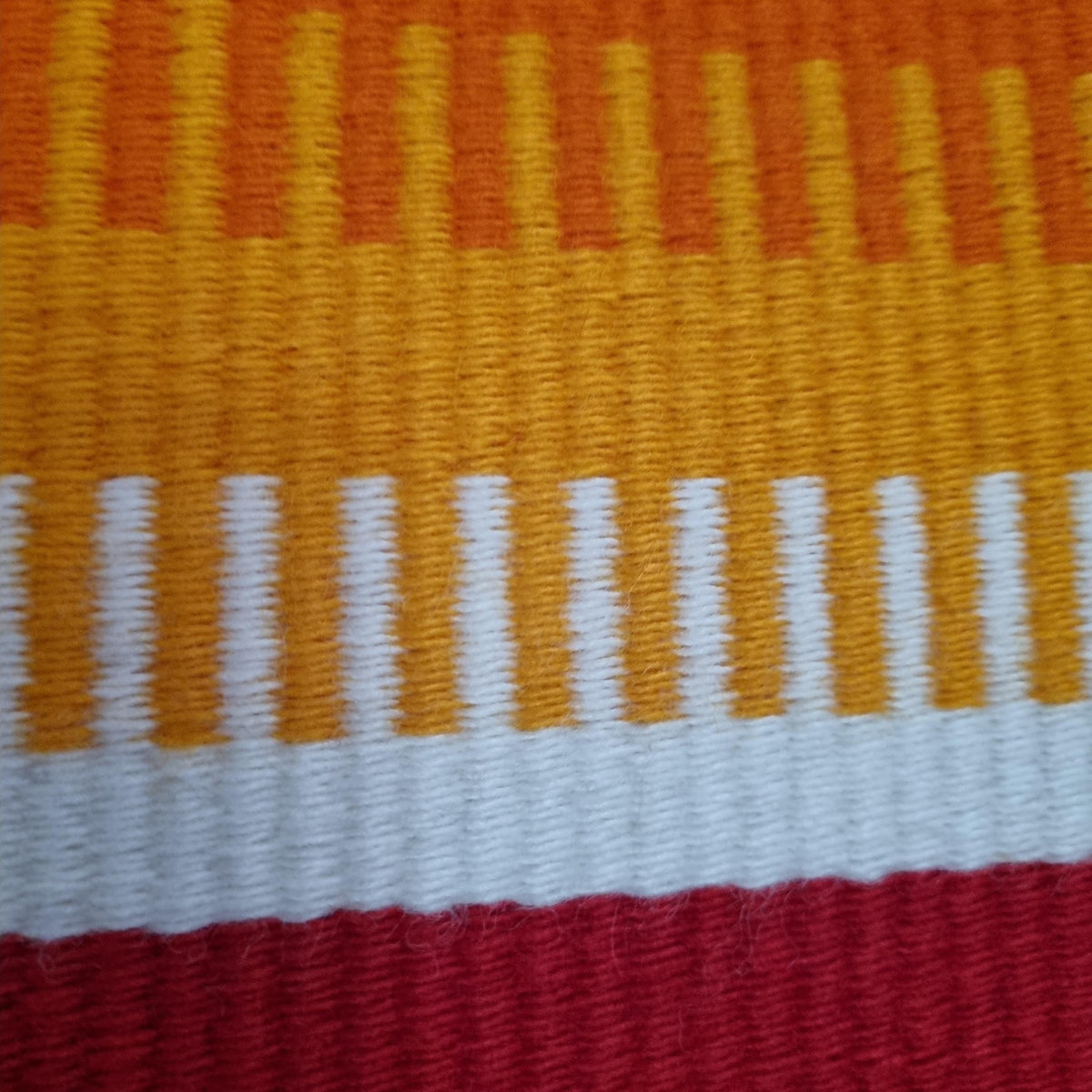 The image is a close-up of a colorful woven fabric with a striped pattern in shades of orange, yellow, and white.