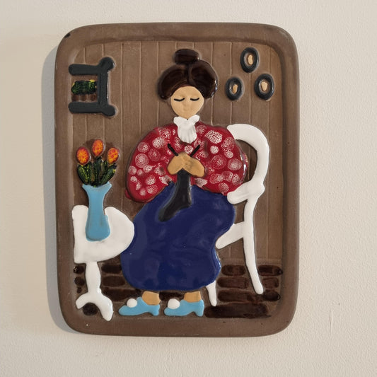 Vintage Swedish Wall Plaque: Helsingborg Pottery Lady Deco 327 featuring a woman knitting in traditional attire with floral decor.